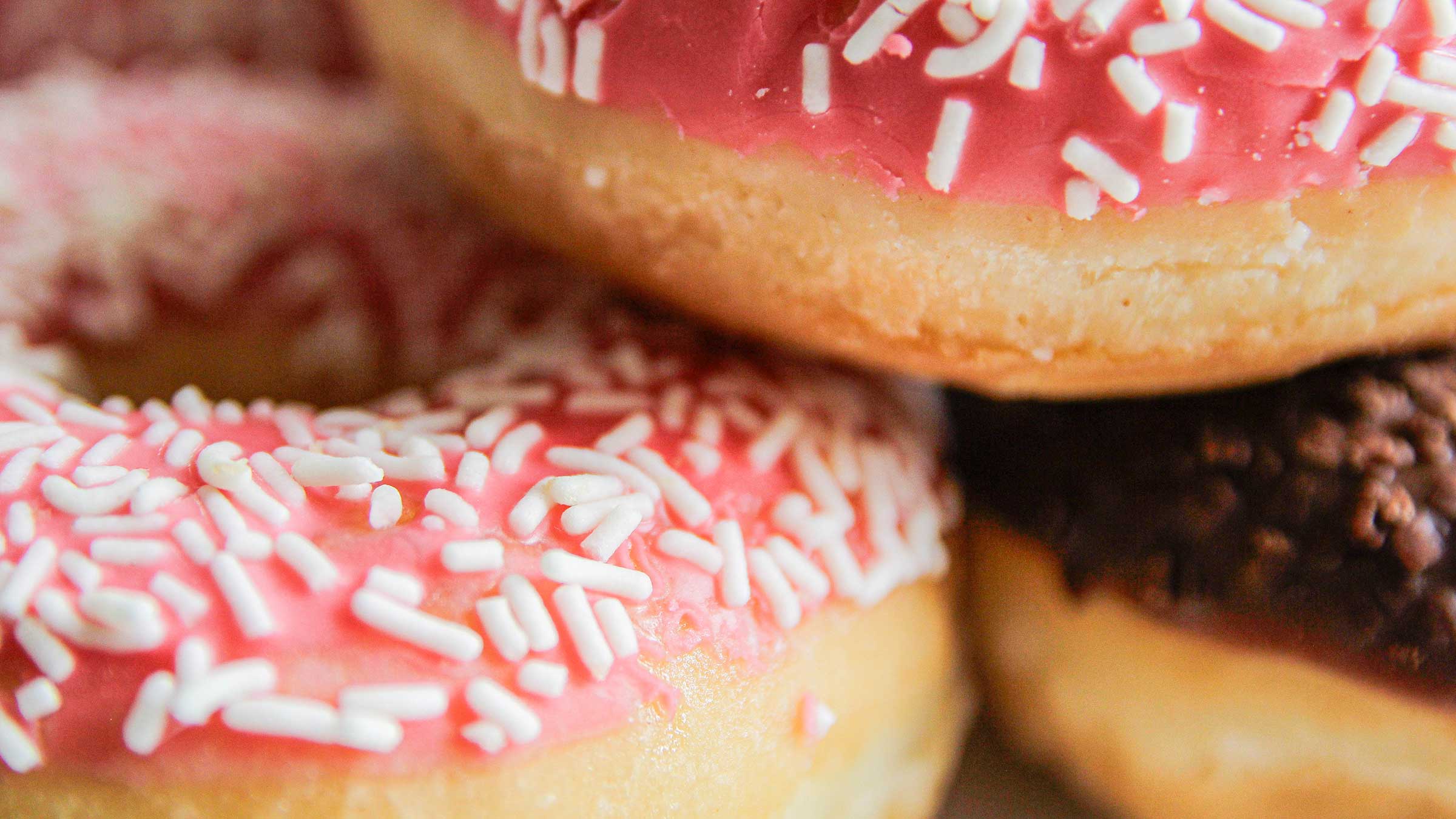A close-up image of pink frosted donuts with sprinkles